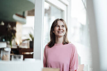 Happy young woman with brown hair looking away while sitting in cafe - JOSEF05287