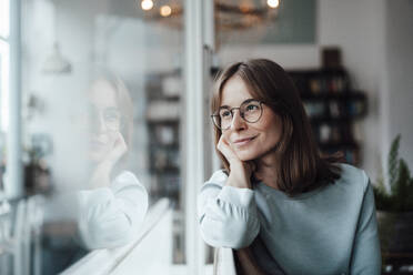 Smiling thoughtful woman with brown hair looking through window while sitting in cafe - JOSEF05308