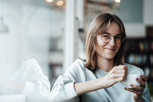 Smiling young woman with coffee cup sitting in cafe - JOSEF05314