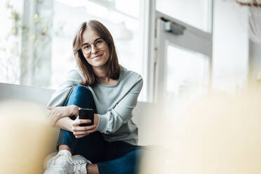 Smiling woman sitting with mobile phone in coffee shop - JOSEF05318