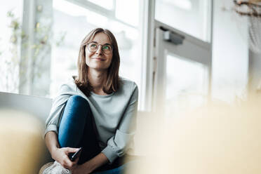 Smiling woman wearing eyeglasses looking away while sitting in cafe - JOSEF05319