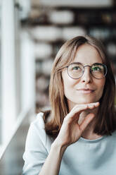 Junge Frau mit Brille sitzt mit der Hand am Kinn in einem Cafe - JOSEF05321