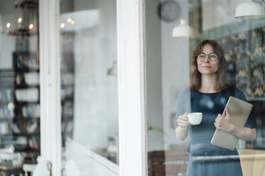 Geschäftsfrau mit Kaffeetasse und Laptop in einem Café, gesehen durch ein Glasfenster - JOSEF05331