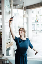 Junge Geschäftsfrau nimmt Selfie durch Smartphone im Café - JOSEF05335