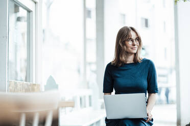 Young female professional looking away while sitting with laptop at cafe - JOSEF05338