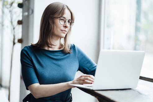 Businesswoman contemplating while sitting with laptop in cafe - JOSEF05340