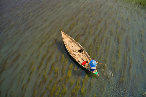 Luftaufnahme eines Fischers, der einen traditionellen Hut trägt und auf dem bengalischen Fluss in der Nähe der Stadt Ullahpara, Rajshahi, Bangladesch, fährt. - AAEF10875