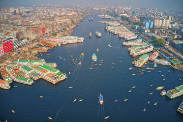 Luftaufnahme mehrerer im Bau befindlicher Boote, die am Buriganga-Fluss in Keraniganj angedockt sind, mit der Skyline der Stadt im Hintergrund, Dhaka, Bangladesch. - AAEF10913