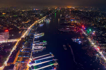 Luftaufnahme des Buriganga-Flusses und des Sadarghat-Terminals bei Nacht mit mehreren angedockten Schiffen und dem alten Stadtteil Dhaka im Hintergrund, Dhaka, Bangladesch. - AAEF10924