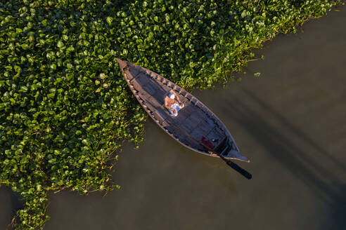 Luftaufnahme eines allein betenden Mannes in einem kleinen traditionellen Kanu auf dem Buriganga-Fluss in der Provinz Dhaka, Bangladesch. - AAEF11031