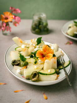 Leckerer Melonensalat mit Gurken und Oliven, serviert auf einem Teller mit Kräutern neben Salzstreuer und Serviette - ADSF27734