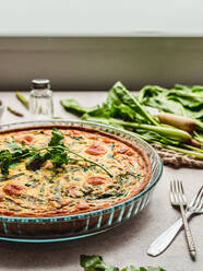 Leckere Quiche mit Petersilie neben Ei und frischem Spinat mit Spargel auf dem Tisch - ADSF27736