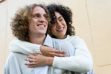 Cheerful man giving piggyback ride to diverse female friend both with curly hair laughing loud - ADSF27755