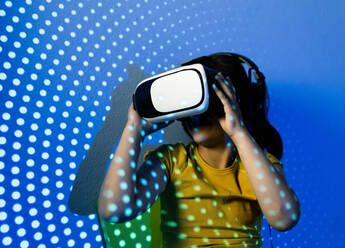 Fröhliches Mädchen mit VR-Headset sitzt mit Neonlichtern im Studio - ADSF27784