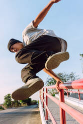 Niedriger Winkel furchtloser junger Mann springt über Metallgeländer in der Stadt bei der Durchführung Parkour Stunt am sonnigen Tag - ADSF27788