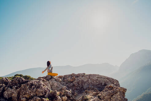 Seitenansicht eines anonymen weiblichen Reisenden, der auf einem Felsen im Hochland sitzt und Yoga in Padmasana macht - ADSF27789