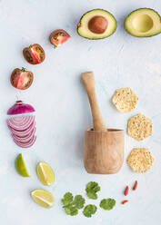 Top view round layout with Haas avocado and tomatoes with fresh greens and wooden mortar for cooking guacamole on white surface - ADSF27793