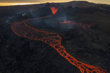 Drohnenansicht eines Stroms heißer orangefarbener Lava, die am Morgen durch bergiges Gelände in Island fließt - ADSF27813