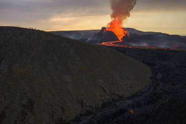 Drohnenansicht eines Stroms heißer orangefarbener Lava, die am Morgen durch bergiges Gelände in Island fließt - ADSF27814