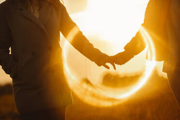Faceless Freundinnen halten die Hände sanft stehen in Objektiv Flare von Sonnenuntergang Licht in der Natur - ADSF27819