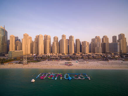 Luftaufnahme des AquaFun-Wasserparks, aufblasbare Wasserrutschen am Strand von Dubai Marina mit Skyline im Hintergrund, Dubai, Vereinigte Arabische Emirate. - AAEF11281