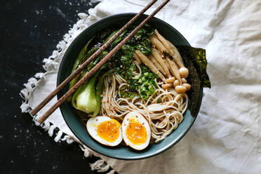 Draufsicht auf eine Keramikschüssel mit leckeren Ramen und Essstäbchen auf einem Tisch mit weißem Tischtuch - ADSF27837