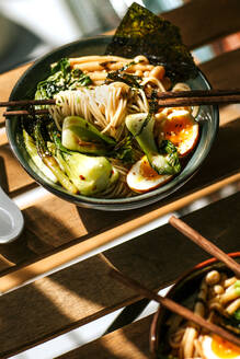 Von oben Schüssel mit leckerem Ramen zum Mittagessen auf Holztisch in Cafeteria platziert - ADSF27839