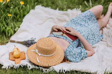 Hohe Winkel von unerkennbaren weiblichen in Kleid mit Strohhut auf Gesicht liegend mit offenem Buch auf Picknick-Decke beim Chillen allein und genießen Sommer-Wochenende in der Landschaft - ADSF27843