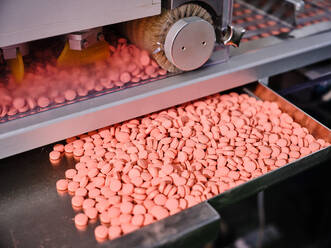 Contemporary pharmaceutical machine with piles of pink pills on conveyor placed in manufacturing laboratory - ADSF27848