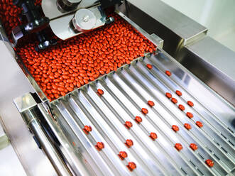 Contemporary pharmaceutical machine with piles of pink pills on conveyor placed in manufacturing laboratory - ADSF27850