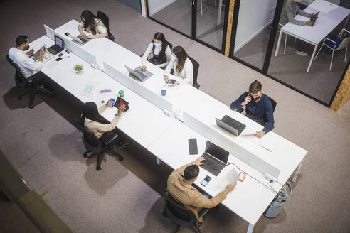 Von oben auf eine Gruppe von Menschen, die an einem Tisch sitzen und Laptops benutzen, während sie im Coworking Space arbeiten - ADSF27853