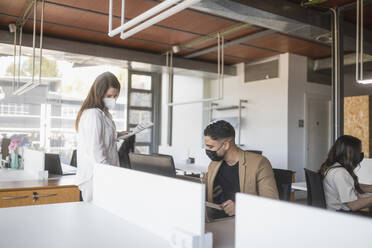 Male and female coworkers in protective masks working on project in spacious workplace - ADSF27895