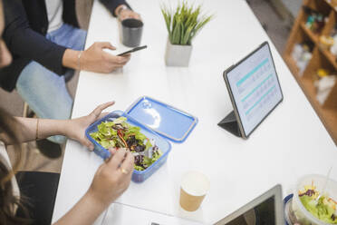 From above of group of unrecognizable coworkers gathering at table ad eating lunch in workplace - ADSF27903