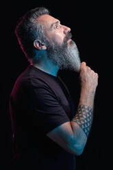 Seitenansicht eines gut aussehenden reifen Mannes mit grauem Bart auf schwarzem Hintergrund im Studio - ADSF27920