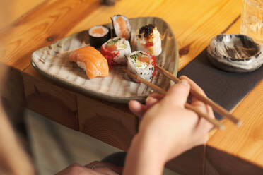 Von oben abgeschnittene unerkennbare Frau isst leckeres Sushi in einem japanischen Restaurant, während sie an einem Holztisch sitzt - ADSF27929