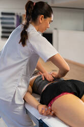 Side view of friendly masseuse smiling and massaging shoulders of woman while working in physiotherapy clinic - ADSF27971