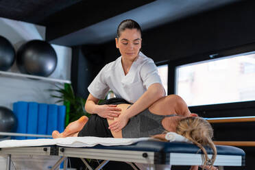 Therapeutin in weißem Gewand massiert den Rücken einer Frau während einer Osteopathiesitzung in einer Klinik - ADSF27977