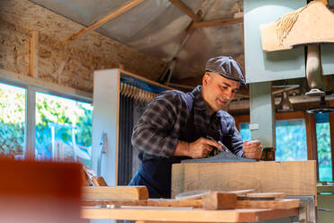 Seitenansicht eines männlichen Holzarbeiters, der ein Holzteil mit einem Hobel glättet, während er in einer professionellen Schreinerei arbeitet - ADSF27986
