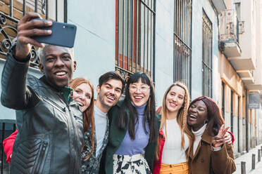 African American male taking selfie with smartphone with company of multiracial friends standing on street together - ADSF28017