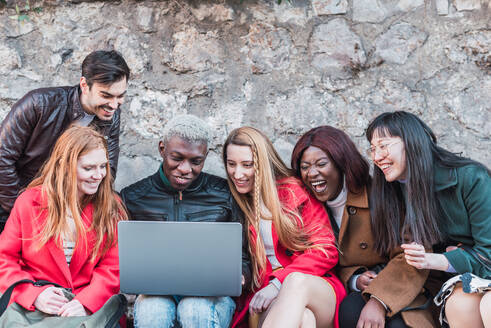 Eine Gruppe verschiedener Studenten macht gemeinsam Hausaufgaben, während sie ein Netbook in einer Straße in der Stadt benutzen - ADSF28035