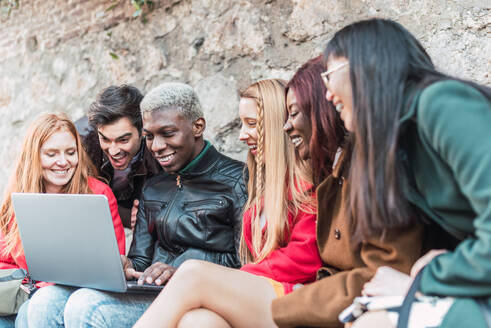 Eine Gruppe verschiedener Studenten macht gemeinsam Hausaufgaben, während sie ein Netbook in einer Straße in der Stadt benutzen - ADSF28036