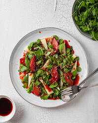 Draufsicht auf einen köstlichen Salat mit Rucola und Quitten, der auf einem Teller mit Soße auf dem Tisch serviert wird - ADSF28070