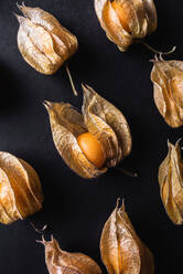 Draufsicht auf einen nahtlosen Hintergrund aus orangefarbenen Physalis, die in Reihen auf einem schwarzen Tisch angeordnet sind - ADSF28071