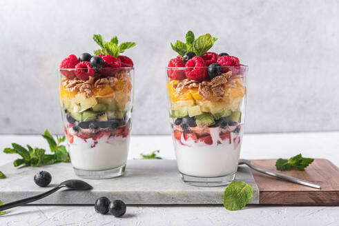 Appetitlicher Joghurt mit Schichten von frischen Früchten, serviert in Gläsern auf dem Tisch mit Minzblättern - ADSF28074