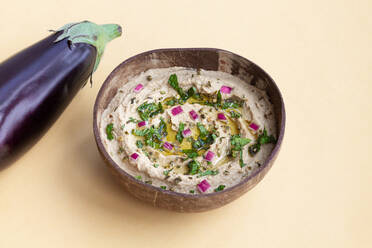 Frische reife Auberginen auf einem beigen Tisch mit einer Schüssel mit dem appetitlichen traditionellen Gericht Baba Ghanoush - ADSF28078