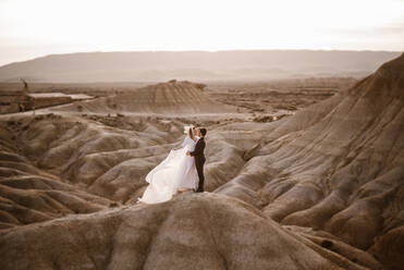 High angle of groom and bride embracing near mountain against cloudy sundown sky in Bardenas Reales Natural Park in Navarra, Spain - ADSF28182