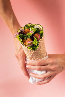 Cropped unerkennbare Person Hände halten vegan Falafel Wrap auf bunten rosa Hintergrund - ADSF28191