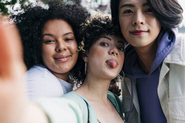 Junge Frau streckt die Zunge heraus, während sie ein Selfie mit multiethnischen Freunden macht - ASGF00861