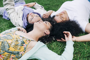 Young male and female friends lying on grass at park - ASGF00877