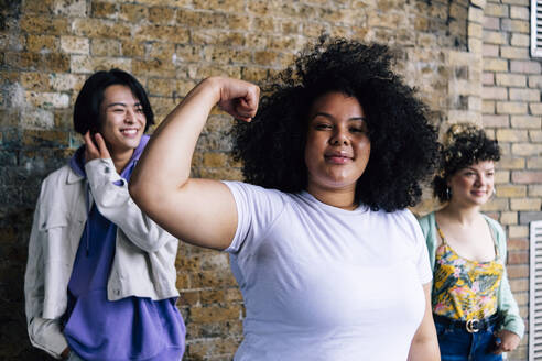 Young woman flexing muscle with male and female friends in background - ASGF00884